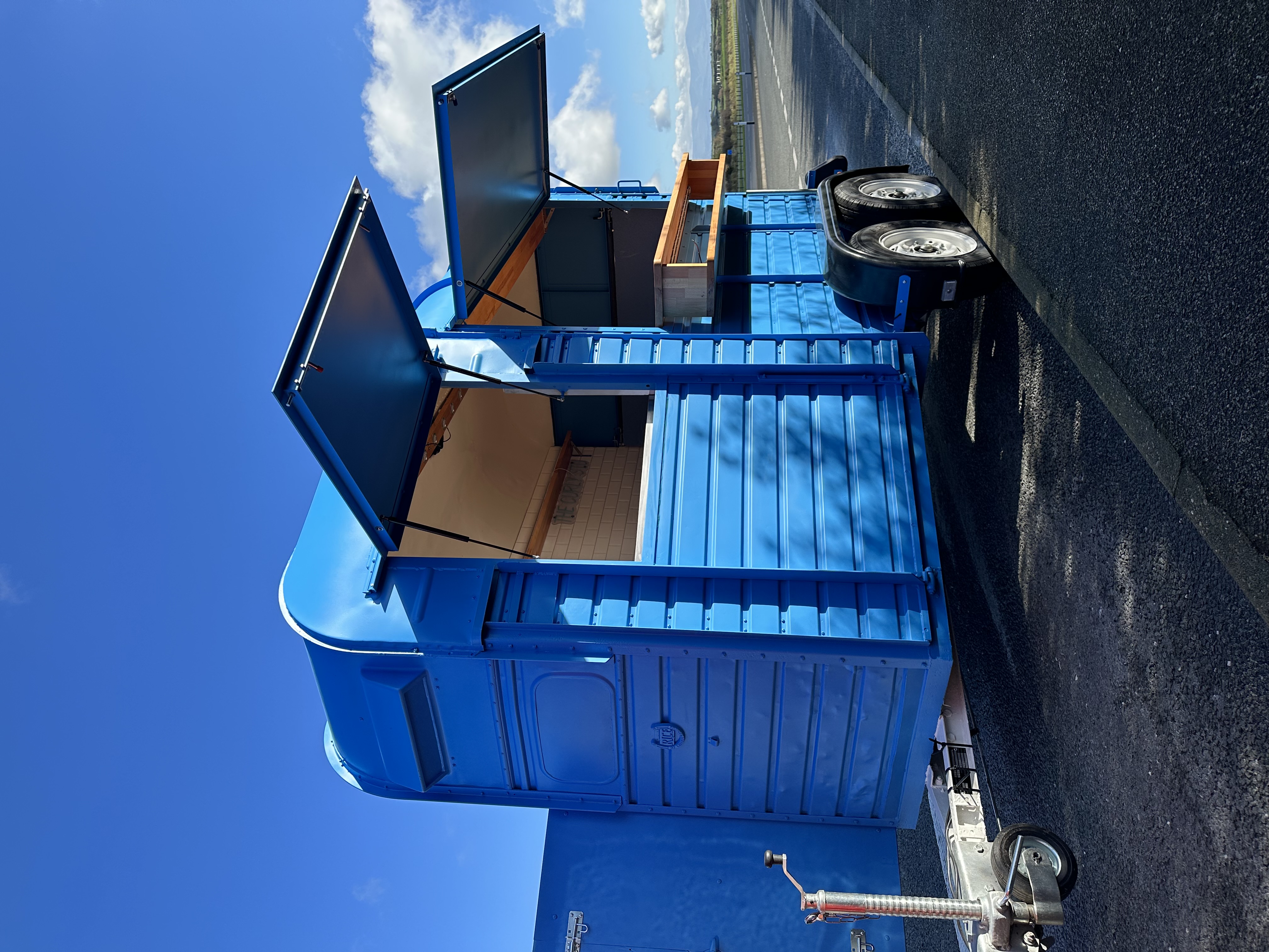 A vivid blue Rice horse trailer converted into a mobile coffee business, hatches open under a blue sky